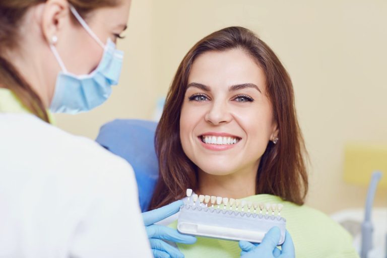 femeie la consultatia de stomatologie pentru refacerea unei coroane dentare, medicul stabileste nuanta coroanei
