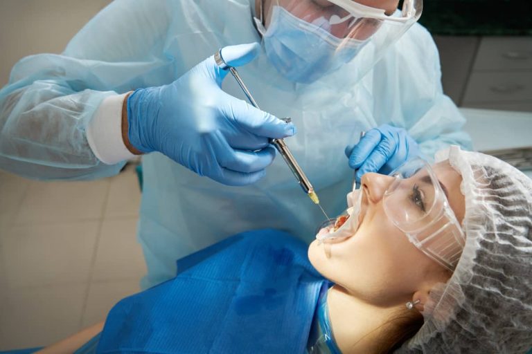 pacienta in cabinetul de stomatologie primeste anestezie locala inaintea interventiei pentru inserarea implantului dentar